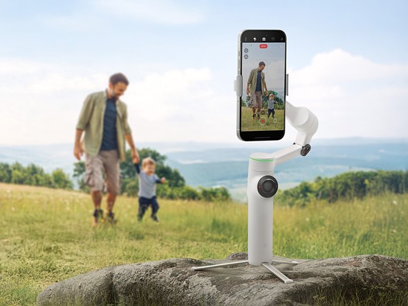 the insta360 flow 2 pro gimbal sits on rock with phone recording man with child in field overlooking hills