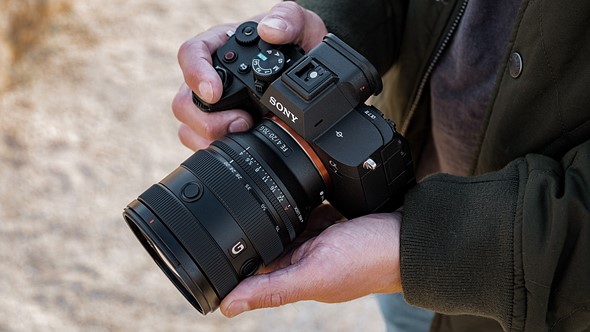 hands hold a mirrorless camera over blurred background