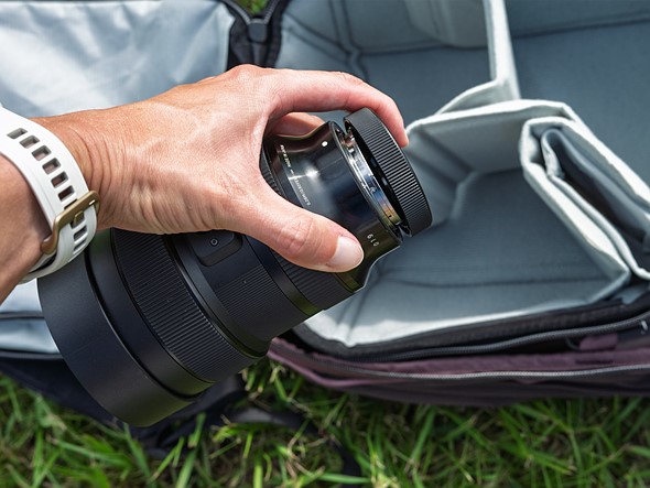a hand holds a lens over a gray camera bag