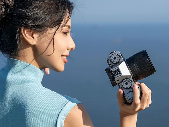 a woman holds a camera with blue ocean in the background