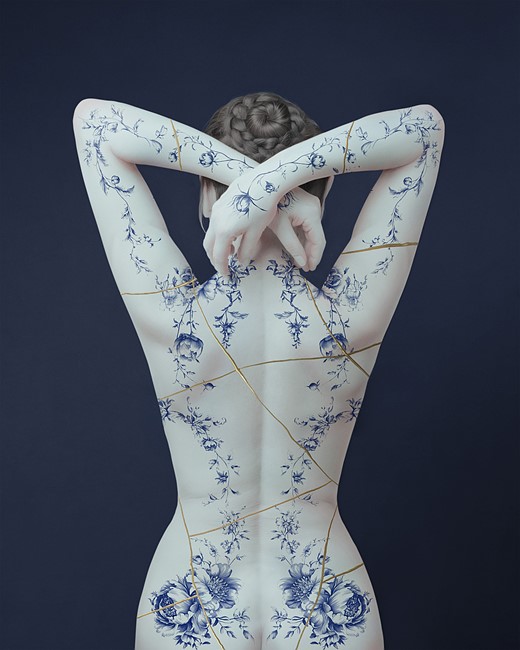 a woman stands with delicate blue flowers painted on her back and gold string criss crossing