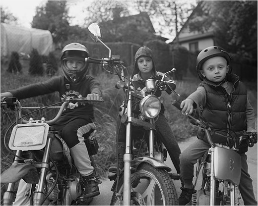 three children sit on motorcycles
