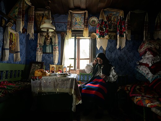 a woman in traditional romanian clothing sits in a dark room filled with fabric and religious items
