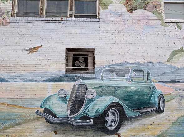 a brick wall is painted with a mural of an old car on a road with mountains in the distance