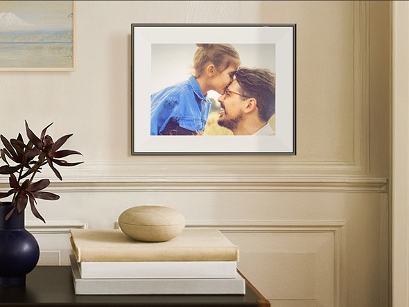 a table with a plant and stack of books sits in front of a tan wall with a picture frame with a candid portrait of a young girl and man
