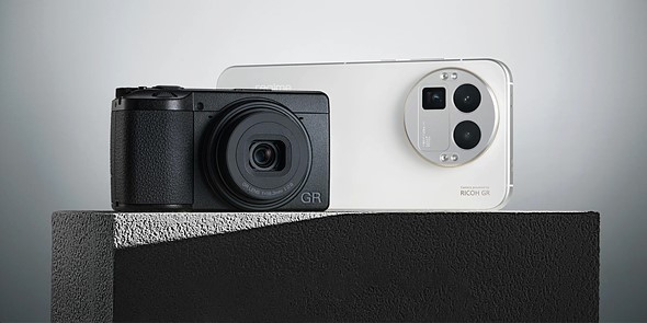 a ricoh gr camera sits on a pedestal in front of a white realme smartphone