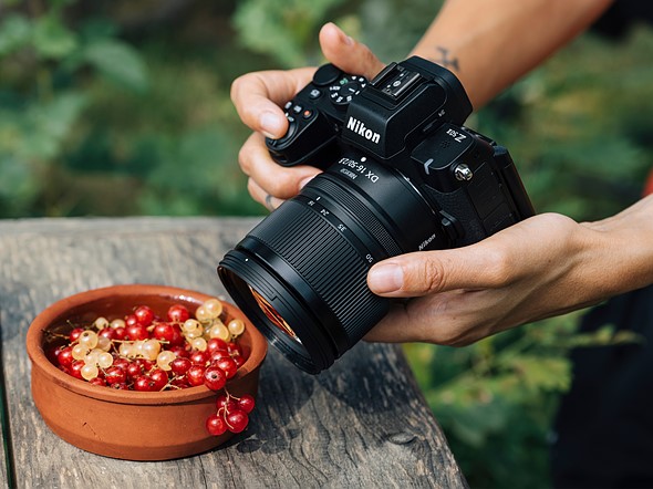 hands hold a nikon camera above a clay bowl of grapes on a wooden table