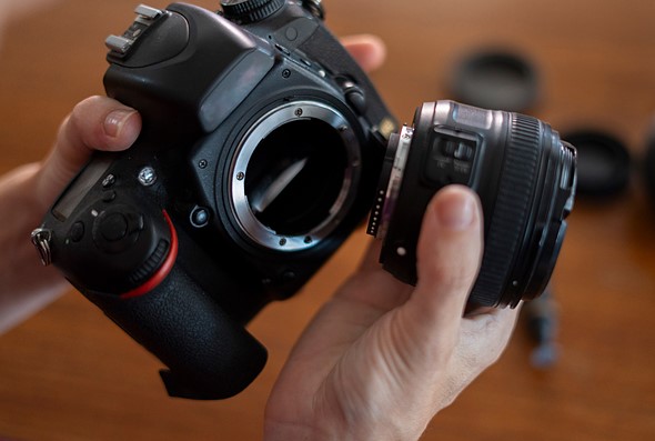 hands hold a camera and lens apart over a brown table