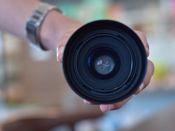 a hand holds a lens with the aperture closed down in front of a blurry background
