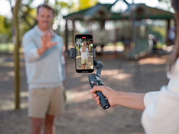 a hand holds the dji osmo mobile 8 gimbal while recording a man in a park
