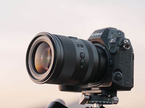 a black nikon camera with a large lens is on a tripod with a soft white background