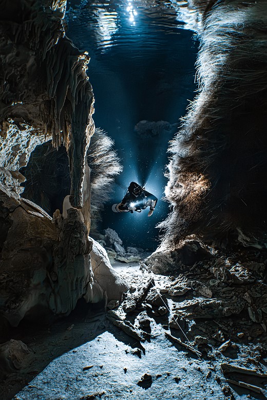 a diver with a flashlight swims through a narrow passage
