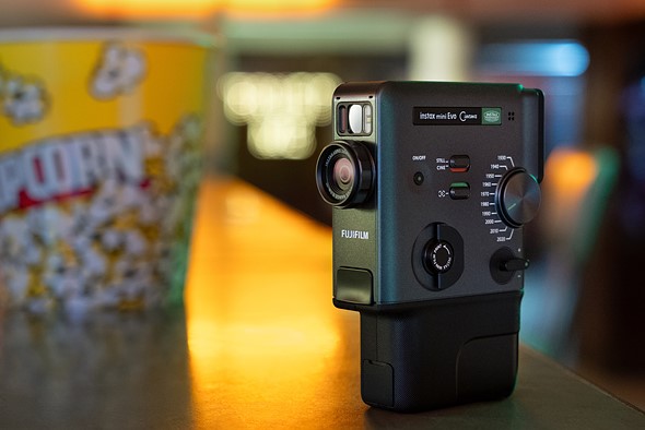 an instax mini evo camera sits on a table with a carton of popcorn in the background