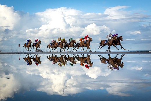 a group rides horses along a reflective pool of water