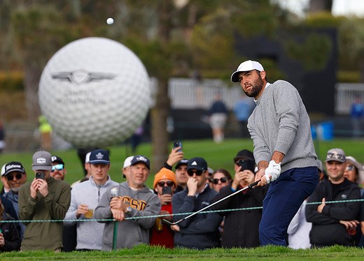 a golfer swings with the ball in the air in front of a crowd