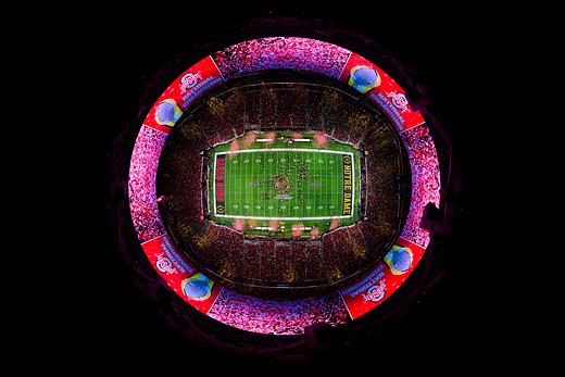 an illuminated football field is in the middle of circular stands at night
