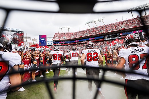 football players run onto a field with a helmet framing the view