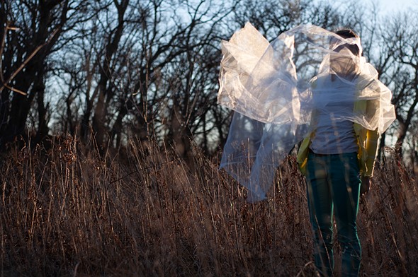 a person wrapped in tulle stands in a field with trees behind her
