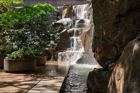 water splashes down a man made waterfall in a courtyard with large potted plants
