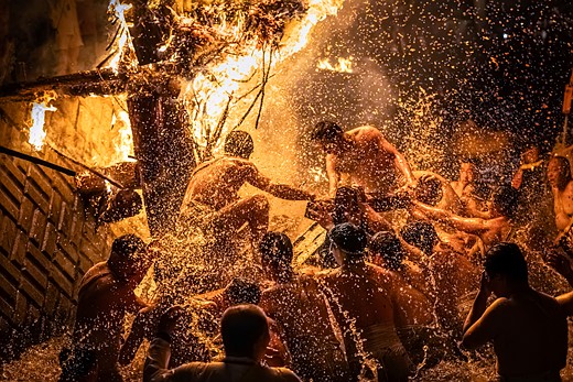 people splash in a river while firey torches send sparks all around