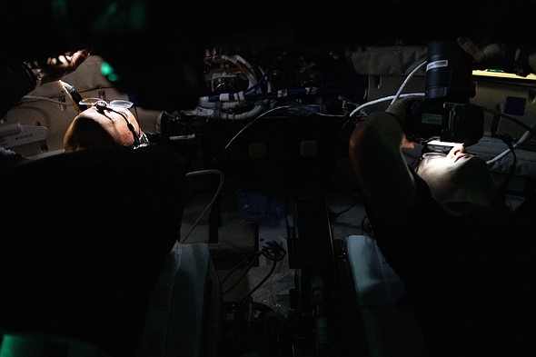 astronauts work in dim light around equipment inside a spacecraft