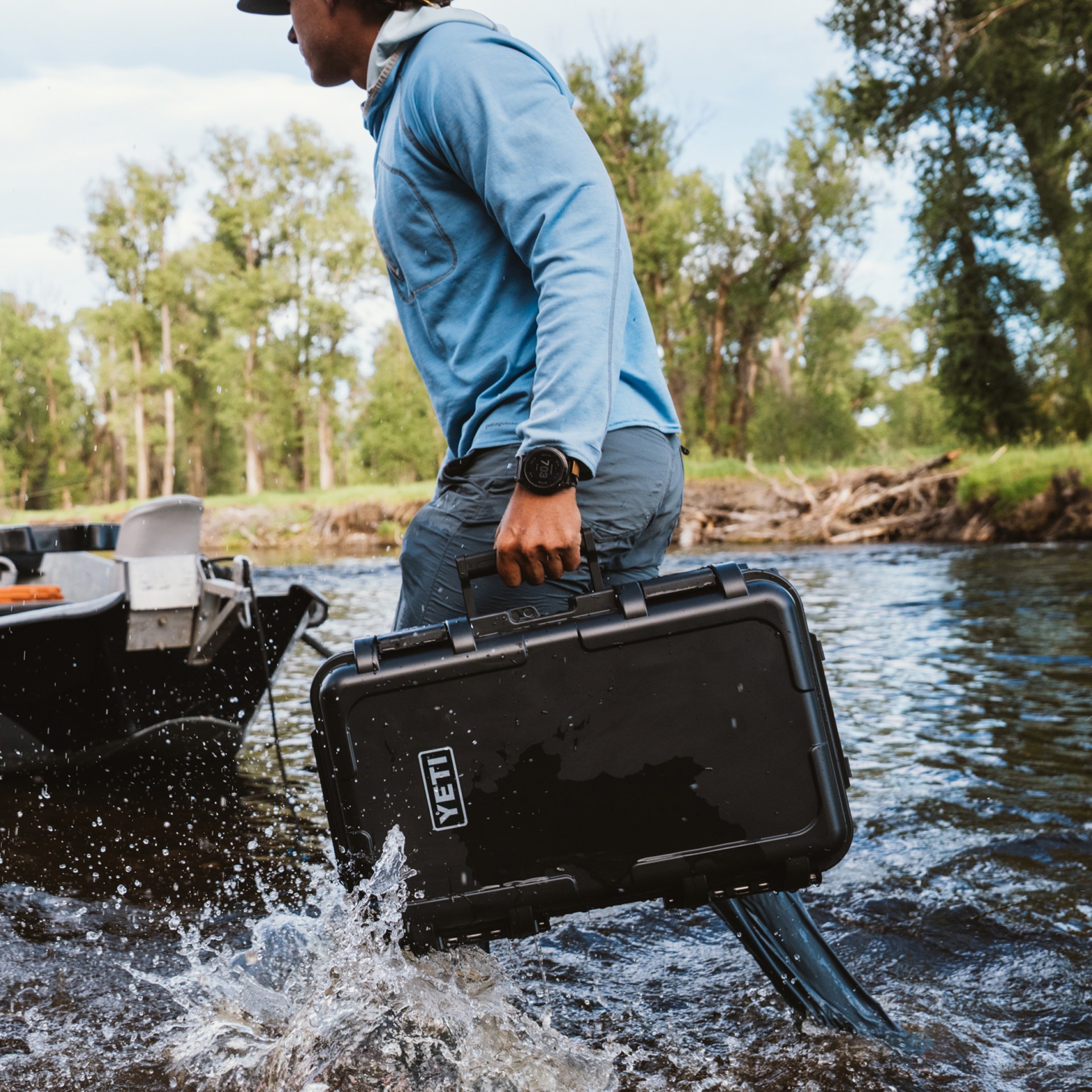 Person wading through a river carrying a black YETI hard case.